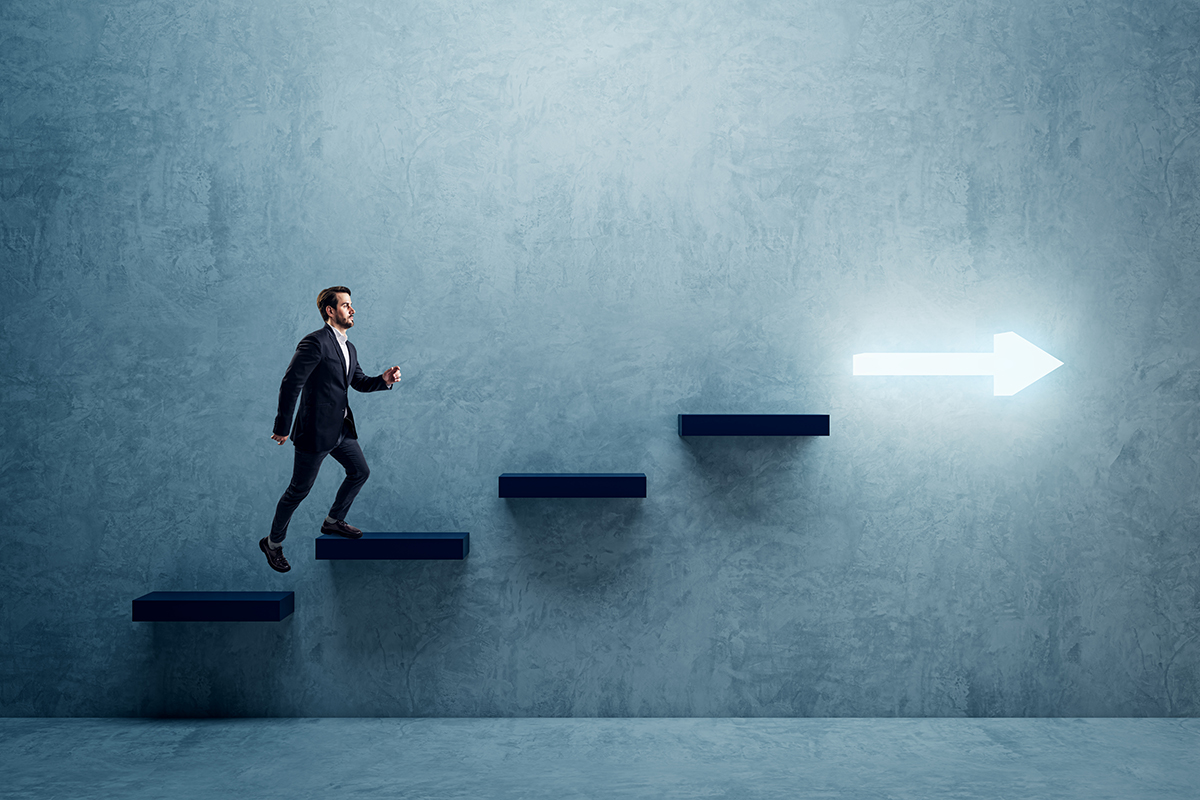 Side view of young business man climbing illuminated arrow stairs to success on concrete wall background in interior. Financial growth, career development and forward concept